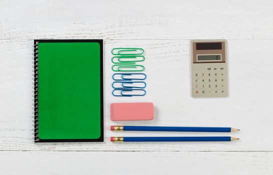 Green spiral notepad with pencils, eraser, calculator, and paper clips on desktop. 