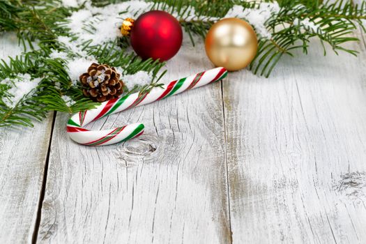 Candy cane with snow covered real Fir tree branches, ornaments, cone and snow on rustic white wooden boards. Christmas season concept. Focus on front part of candy cane. 
