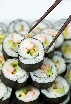 Vertical closeup photo of chop sticks picking up single California hand roll sushi on top of pile of additional sushi 