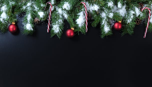 Snowy Christmas tree branches, candy canes and red ornaments on black background 