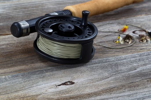 Close up of fly reel, focus on front bottom of reel, with partial cork handled pole and flies blurred out on rustic wooden boards 

