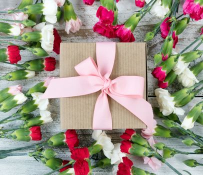 Colorful carnations surrounding gift box on white weathered wooden boards 