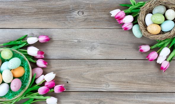Traditional basket and bird nest filled with colorful eggs and pink tulips in both corners on weathered wooden boards for Easter background  