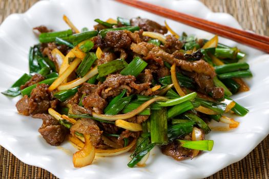 Close up view of beef and green onions in white plate with bamboo mat underneath.  