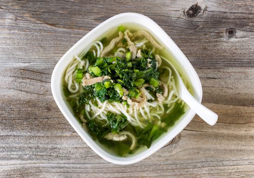 High angled view of noodle and vegetable soup with spoon in bowl on rustic wood. 