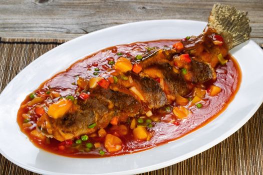 Close up front view of a bread coated fried whole fish in sauce with fruit and vegetables.  