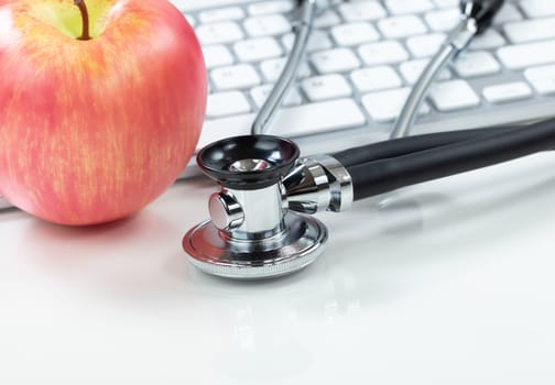 Medical health care concept with traditional stethoscope and apple with computer keyboard in background 