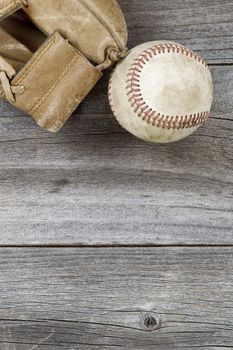 Vertical top view angle of old baseball and weathered leather mitt on rustic wood. Plenty of copy space. 