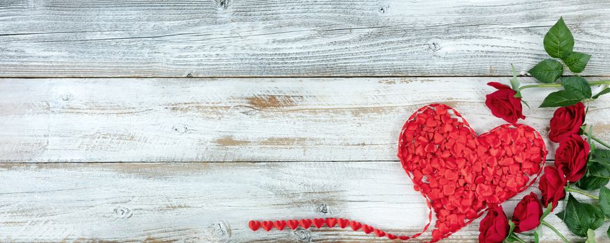 Romantic red roses and filled heart shaped ribbon on white rustic wooden background