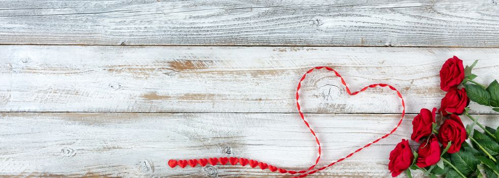 Romantic red roses and heart shaped ribbon on white rustic wooden background