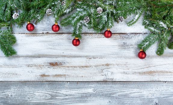 Snowy Christmas fir branches with traditional red ball ornaments and pine cones on rustic wood in flat lay format