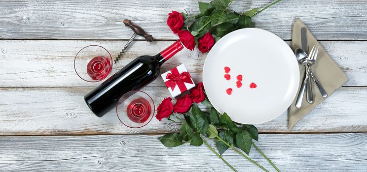 Valentine dinner setting with gift, red roses, wine and heart shapes on rustic table