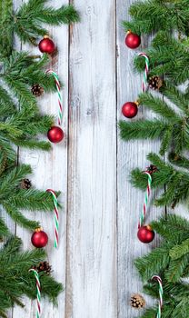 Christmas tree branches, candy canes and red ornaments forming vertical borders on rustic white wood