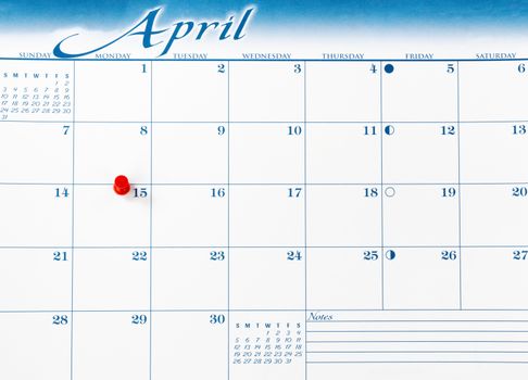 Red pushpin on day of April 15 of calendar for tax income due date reminder in overhead view