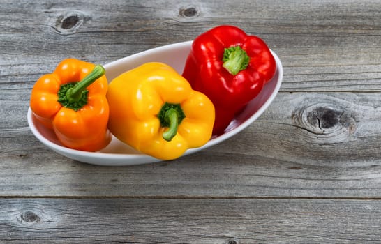Top view angle of three fresh bell peppers, white bowl, on aged wooded boards