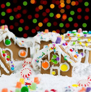 Photo of Gingerbread houses, surrounded by powdered snow, with colorful lights in background on black 