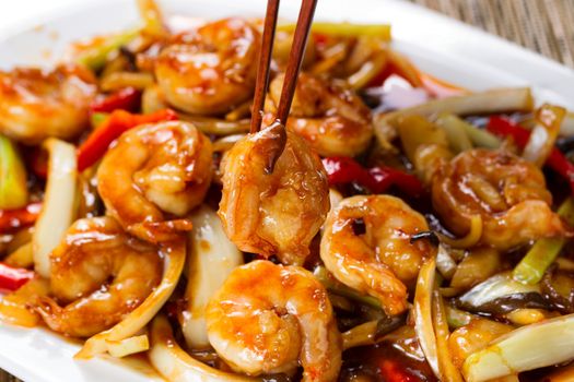 Close up front view of a curry shrimp, selective focus on single piece in chopsticks, with fresh peppers on onion in background. 
