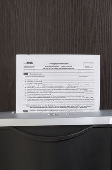 Foreign Earned Income form in shredder with wooden desk in background 