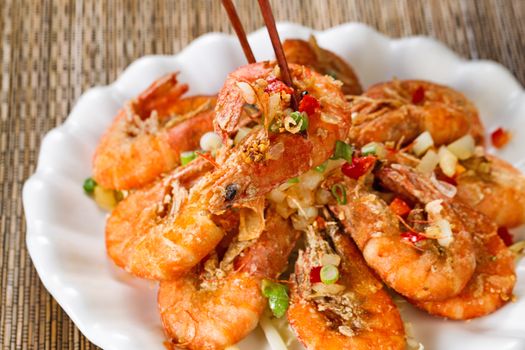 Close up front view of a fried bread coated shrimp, selective focus on single piece in chopsticks, with fresh garnishes. 