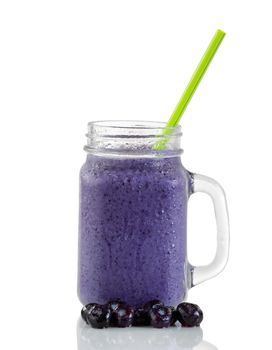 Frosted blueberry smoothie in jar glass with whole berries and green straw isolated on white with reflection.