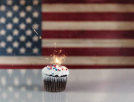 Chocolate cupcake and exploding sparkler with rustic wooden United States Flag in background. July 4th holiday concept