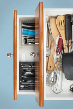 Open Kitchen Drawer with utensils on display with light blue background 