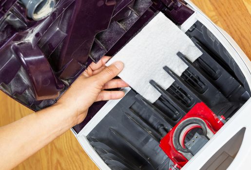 Horizontal photo of female hand installing clean vacuum cleaner filter with hardwood floors in background 