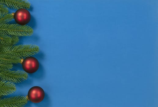 Merry Christmas holiday left fir branches and red ball ornaments border on blue background for the season  