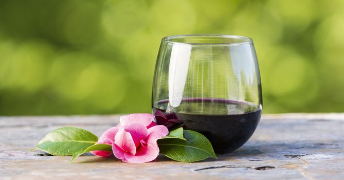 Horizontal photo of red wine in glass and late spring pink flower with bright green background 