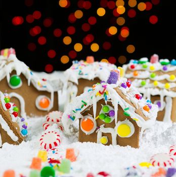 Photo of Gingerbread houses, surrounded by powdered snow, with night lights in background 