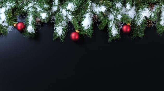 Snowy Christmas branches with red ornaments on black background  