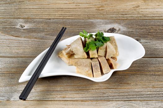 Close up front view of sliced duck meat in small bowl on rustic wood with chopsticks. 