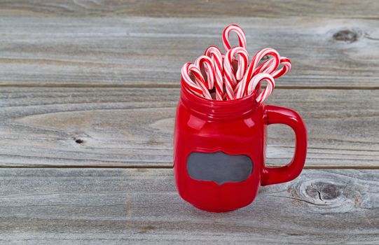 Close up of a red mug filled with Christmas candy canes on rustic wood