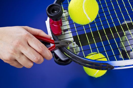 Hand holding pliers while trimming string on tennis racket  on blue background 