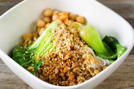 Close up front view of crispy spicy chicken with noodles and bok choy in white bowl. Selective focus in middle of dish. 