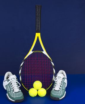 Tennis racket along with tennis shoes and balls on blue background