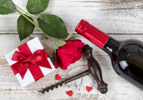 Valentines gift with red wine, rose and corkscrew opener on rustic white wood in overhead view