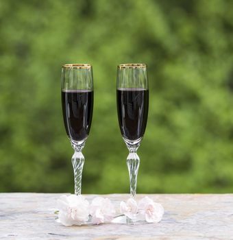 Photo of red wine in glasses with late spring pink flower on bright green background 