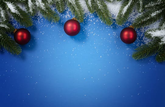 Merry Christmas holiday top circle snowy fir branches and red ball ornaments border on blue background for the seasonal tradition   
