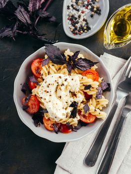 Tasty italian fusilli pasta with cherry, mozarella or buratta cheese and fresh basil. Dish with pasta on black concrete background. Top view. Copy space. Healthy food concept and recipe idea. Vertical