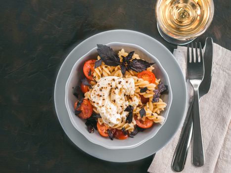 Tasty italian fusilli pasta with cherry, mozarella or buratta cheese and fresh basil. Dish with pasta on black concrete background. Top view. Copy space. Healthy food concept and recipe idea.