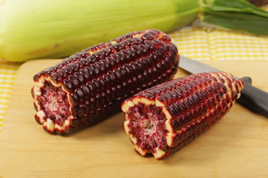 Fresh purple corn fruits on chopping board over napery background. 