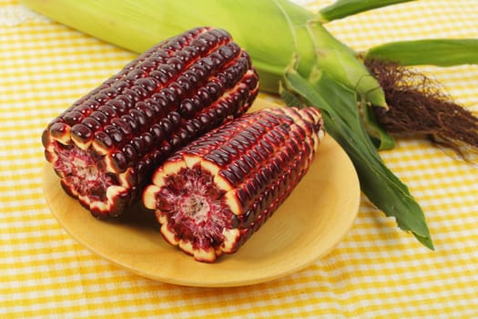 Fresh purple corn fruits on wooden plate over napery background. 