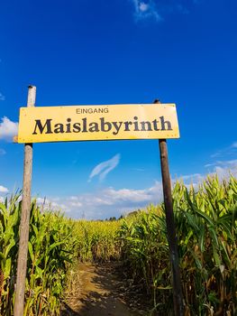 Corn Maze is a maze cut from a corn field. Maize labyrinths are popular with tourists and children. Entrance sign in front of blue sky with lettering in german - entrance Maislabyrinth