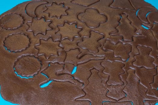 Raw dough is being punched out for the holiday cookies on a blue underlay. Preparing gingerbread cookies. Steps to making biscuits. Top view.