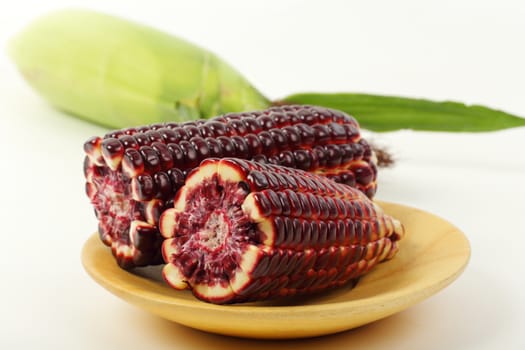 Fresh purple corn fruits isolated on wooden plate over white background. 