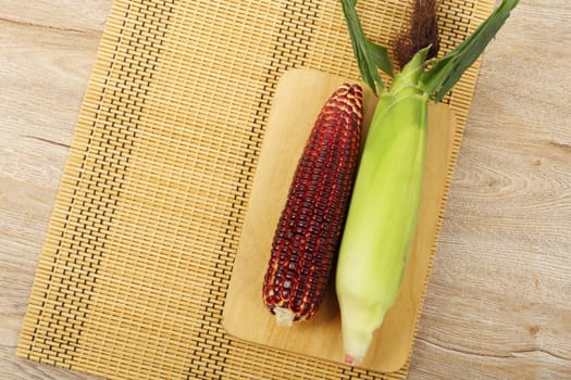 Top view of fresh purple corn fruits on chopping board over wood background. 