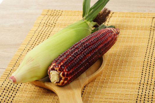 Fresh purple corn fruits on chopping board over wood background. 