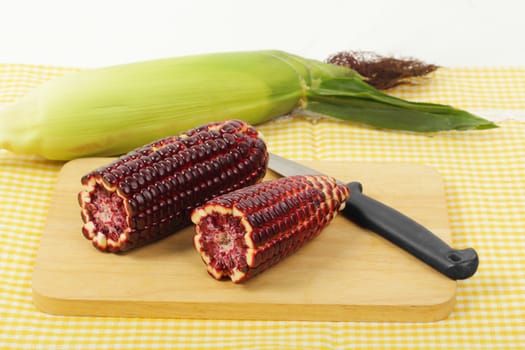 Fresh purple corn fruits on chopping board over napery background. 