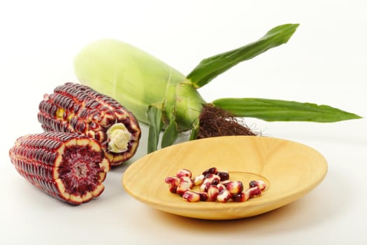 Fresh purple corn fruits isolated on wooden plate over white background. 